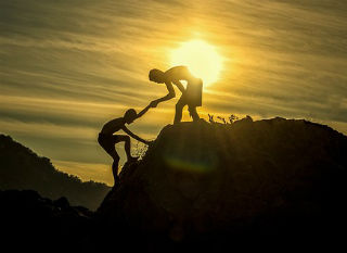Man helping other person up a mountain